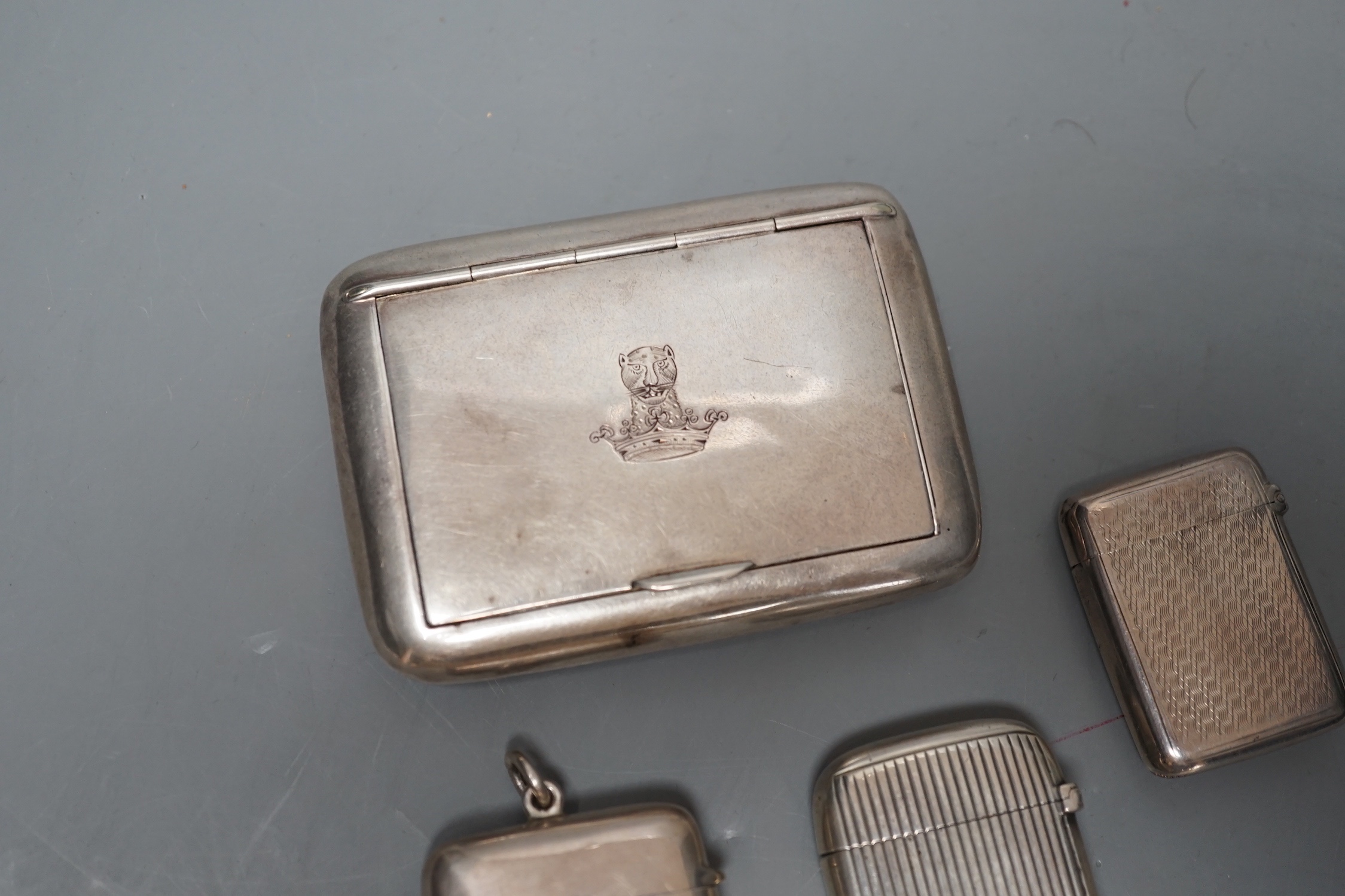 An Edwardian silver snuff box, with engraved crest, Birmingham, 1907, 82mm, three silver vesta cases and an incomplete white metal child's rattle.